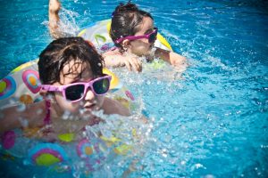 Two children with sunglasses float and splash in a bright blue pool