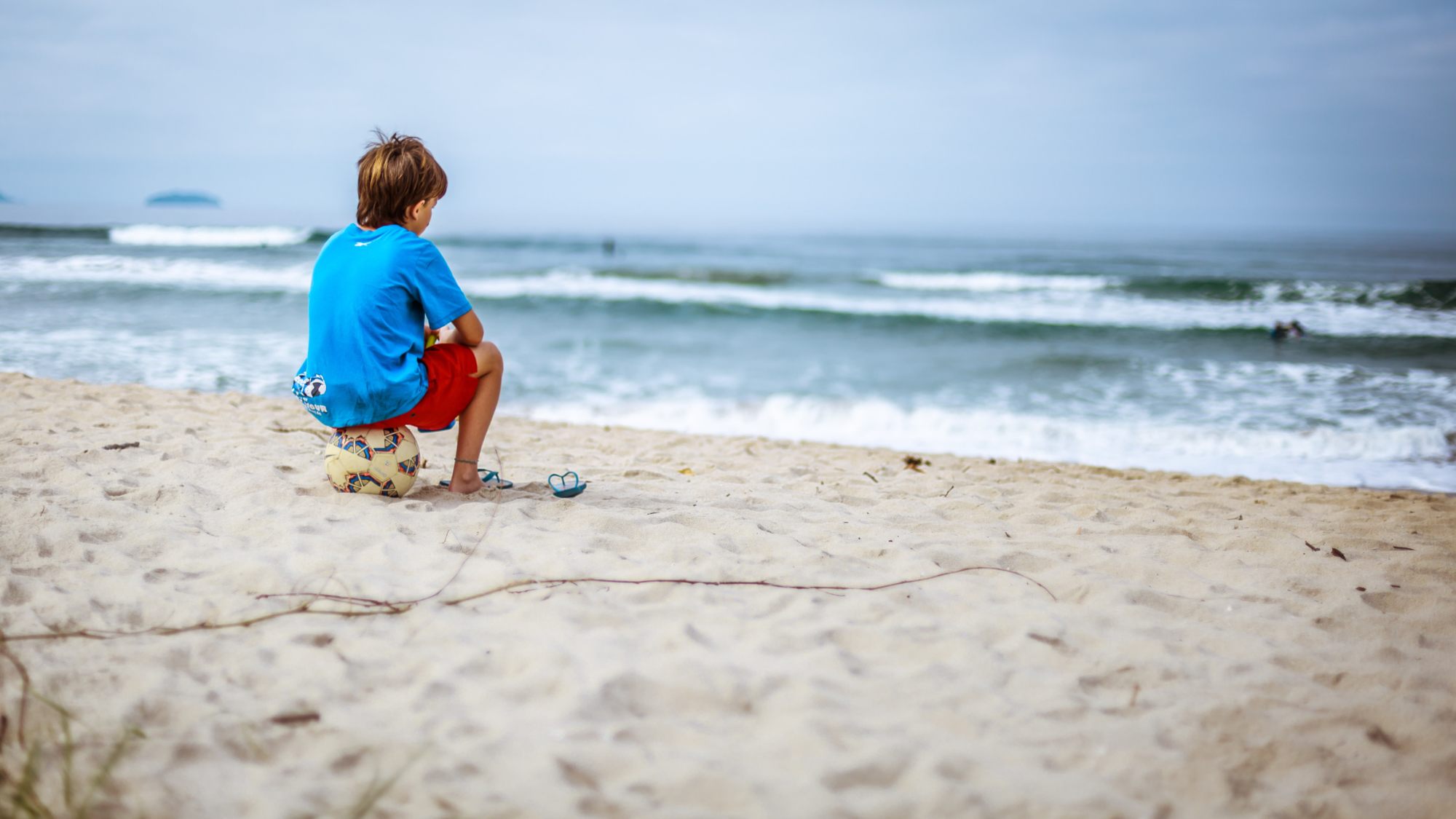 Child at the beach for summer break sitting on a soccer ball